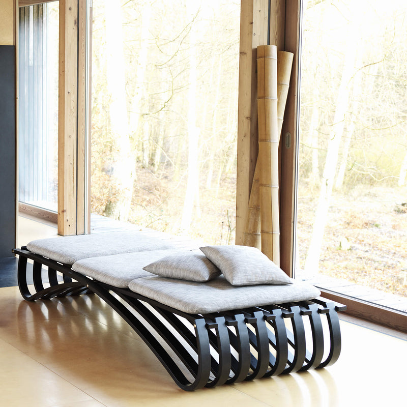 Black daybed with three textile cushions, placed next to a glass door