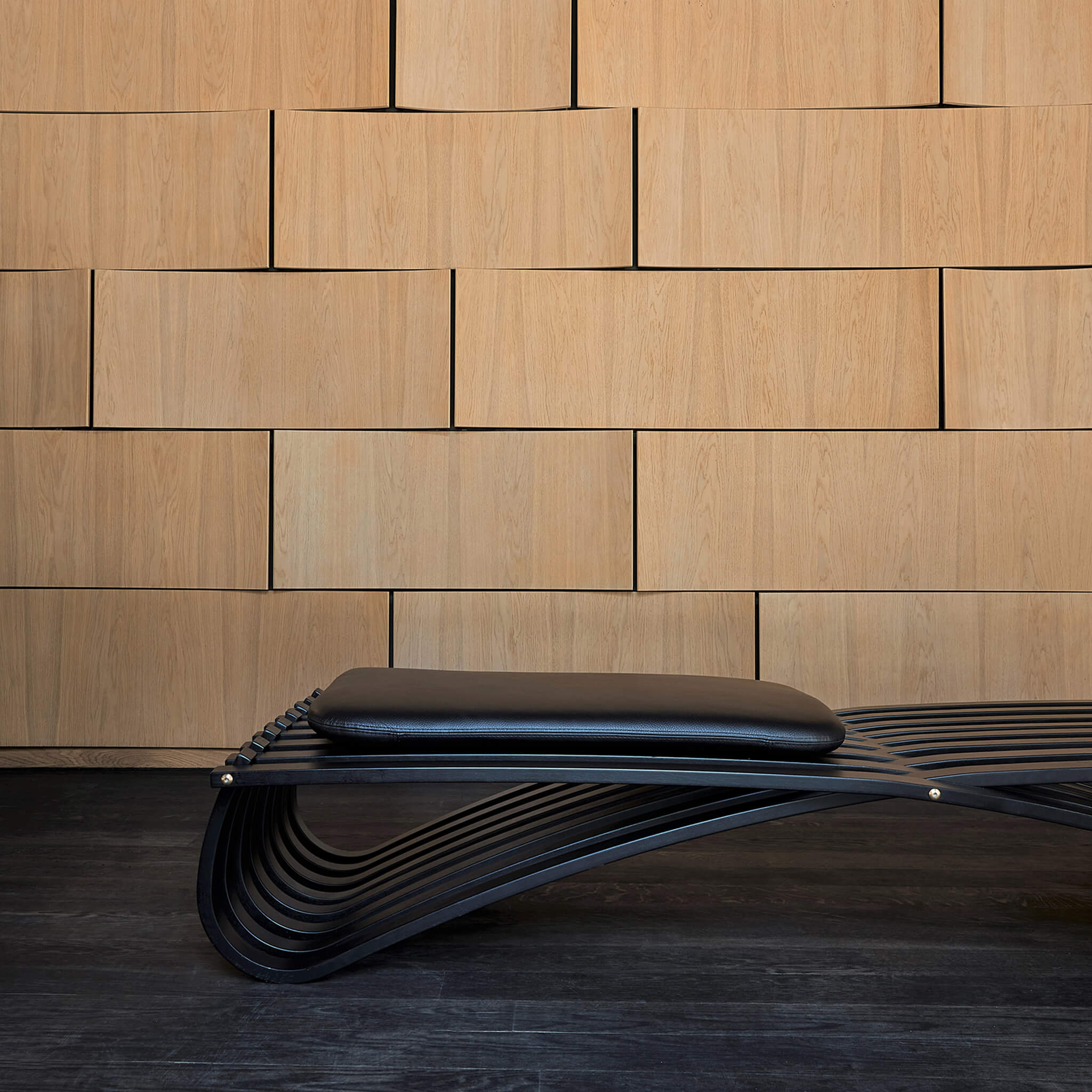 Black daybed with one leather cushion, placed against a wooden wall