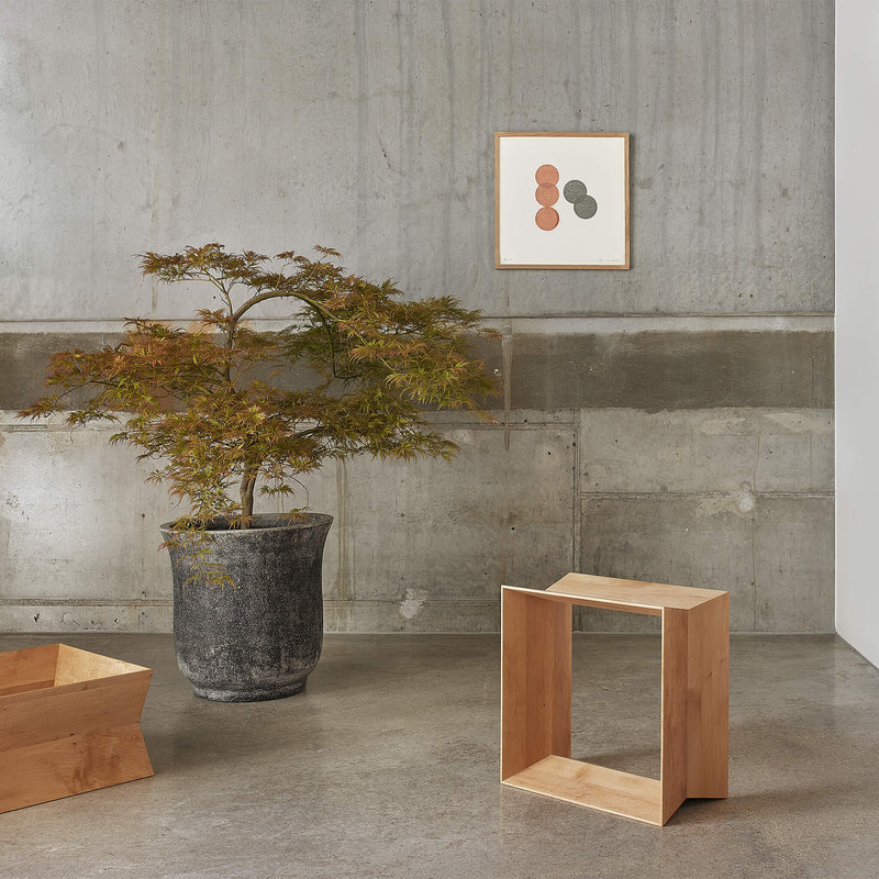 Oak stool placed next to a tall plant, on a concrete floor