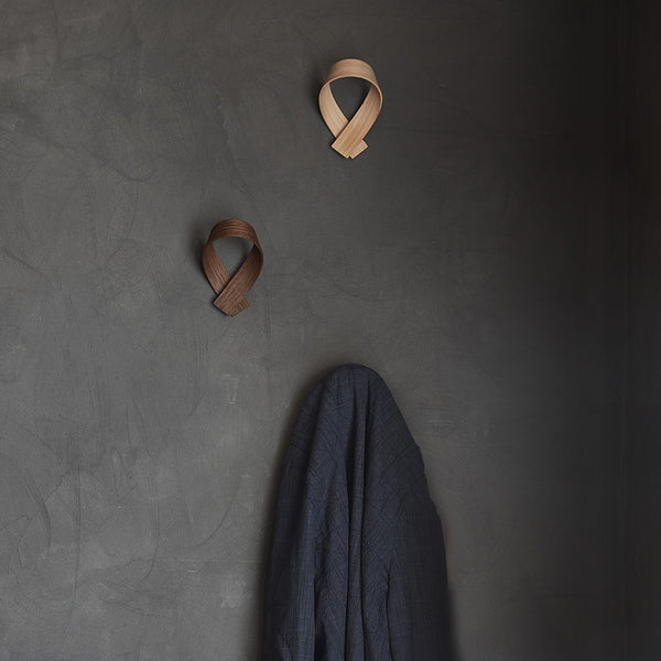 Three coat hooks place on a wall, one holding a jacket