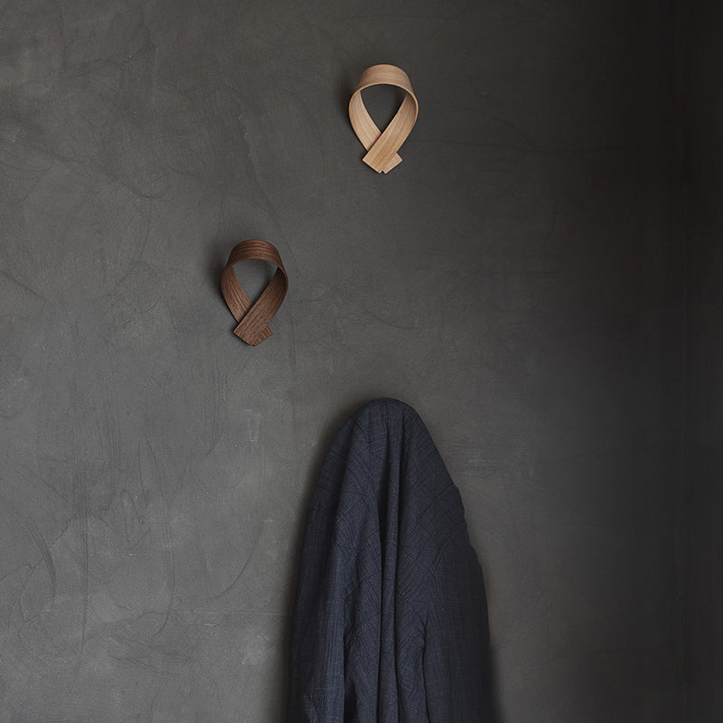Three coat hooks place on a wall, one holding a jacket
