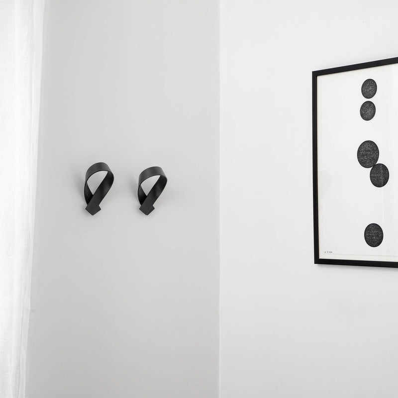 Two black coat hooks on a wall next to a painting