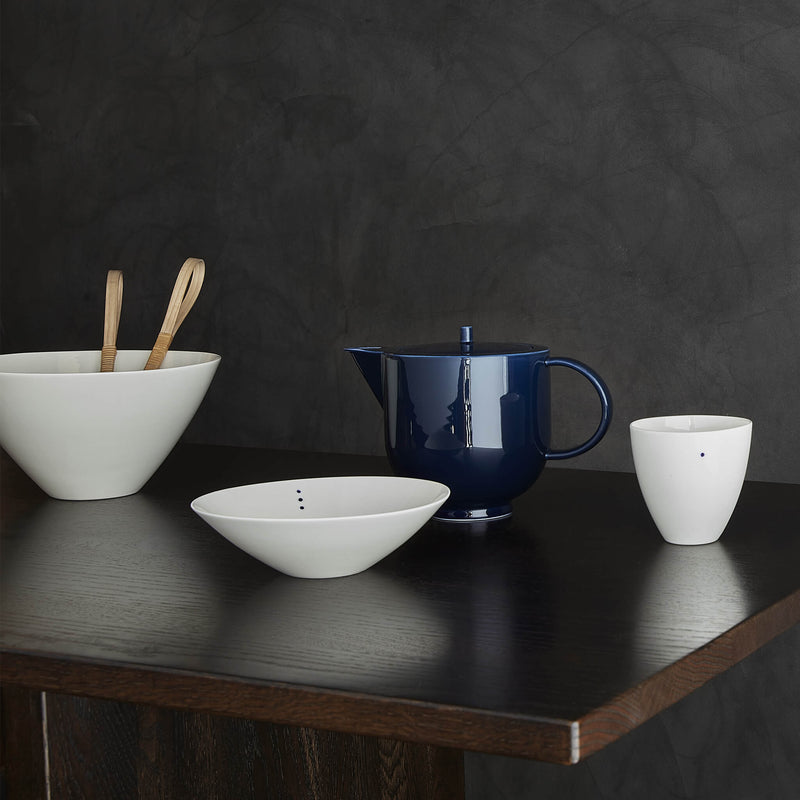 Three porcelain bowls placed on a wooden table, next to a teapot