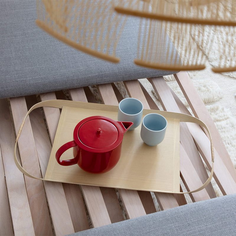 Two tea mugs placed next to a teapot, on a wooden tray, top view