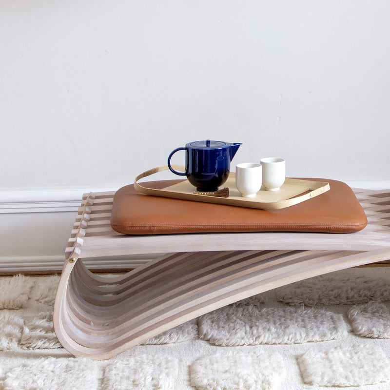 Two tea mugs arranged next to a teapot on a wooden tray, placed on a daybed
