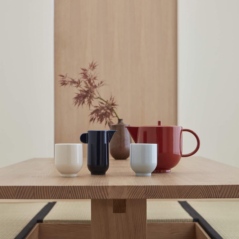 Porcelain tea set placed on a wooden table, in front of a vase