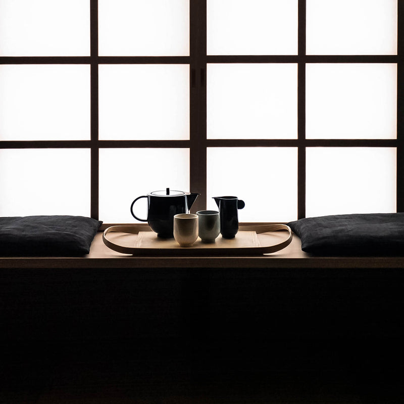 Tea set placed on a wooden tray by the window, in a dark room